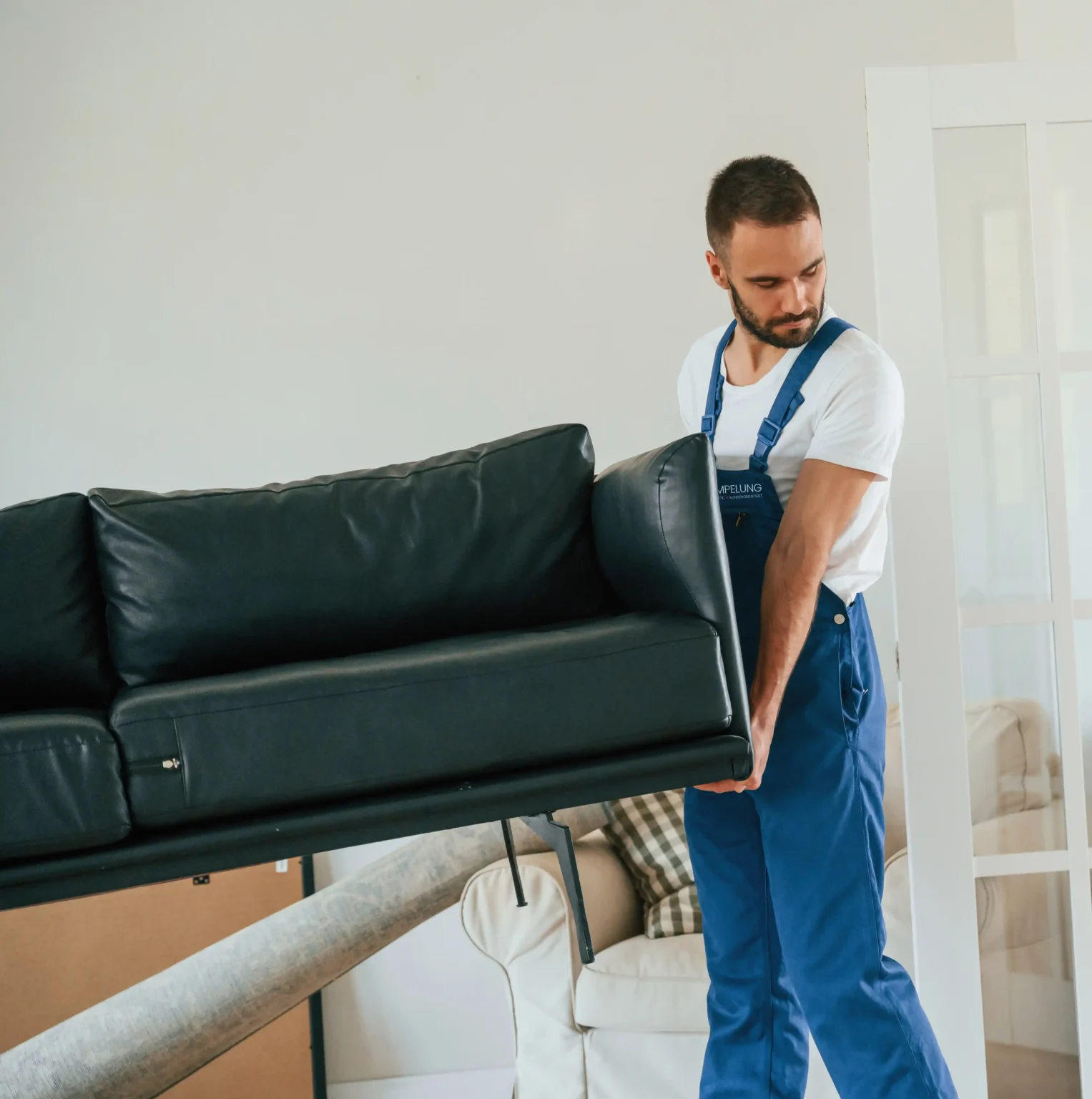Mann in Arbeitskleidung beim Tragen eines Sofas, symbolisch für Haushaltsauflösung in Troisdorf
